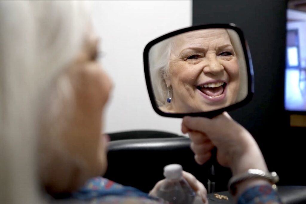 An older woman smiles happily as she admires her teeth in a handheld mirror, reflecting her satisfaction with her dental treatment - Dentist Georgetown TX An older woman smiles happily as she admires her teeth in a handheld mirror, reflecting her satisfaction with her dental treatment - Dentist Georgetown TX